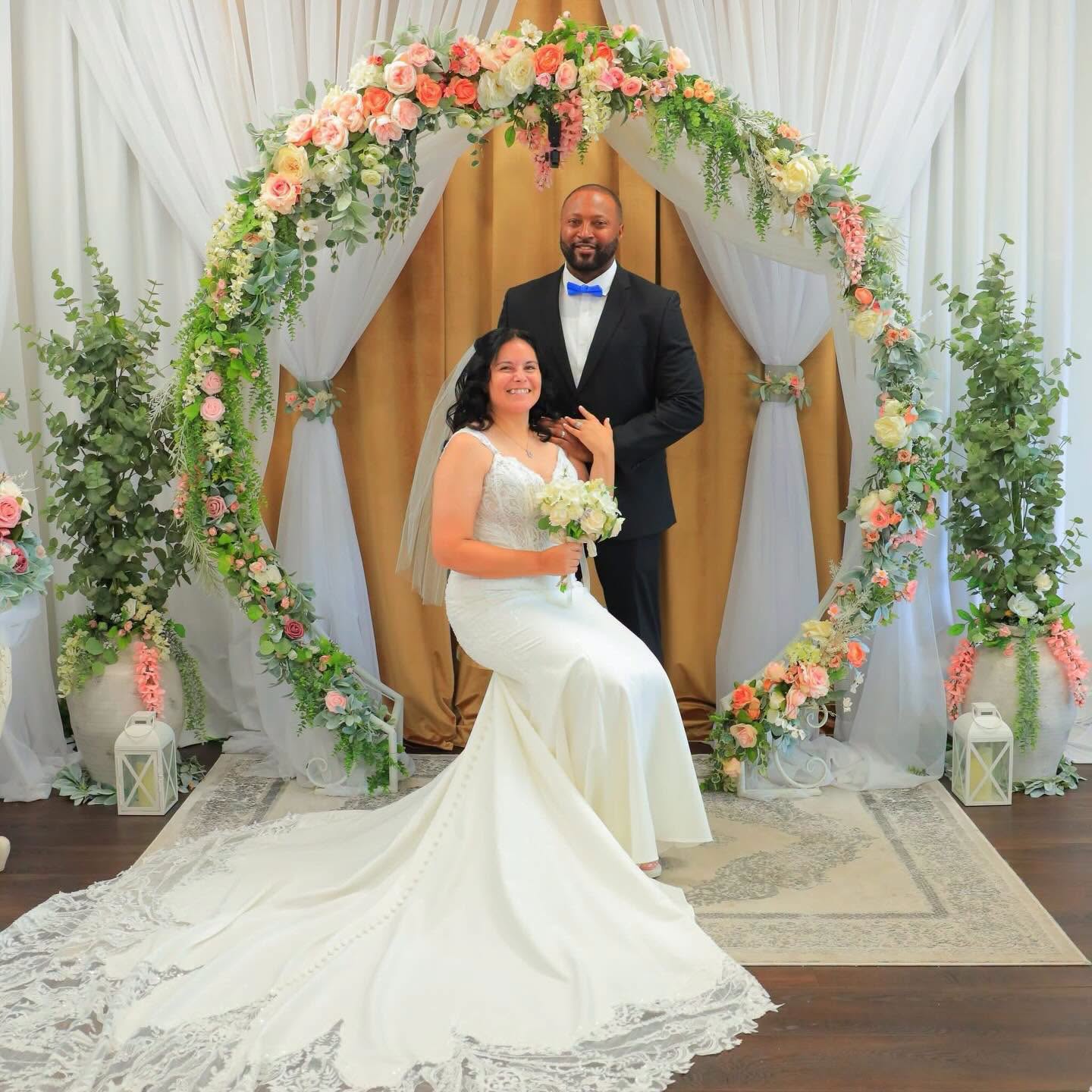 Bride and groom posing beneath the floral arch after their chapel wedding